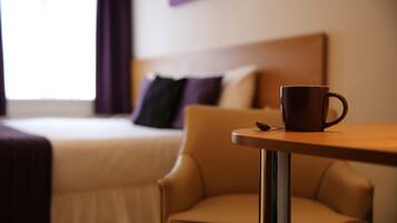A hotel room with a bed, a chair, and a table with a cup.