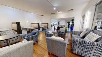 A modern lounge area with seating arrangements, a dining table, and a view of the outdoors.