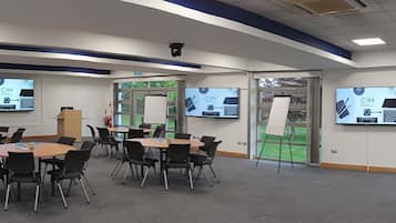 A conference room with multiple tables and chairs, large windows, and screens displaying CIM content.