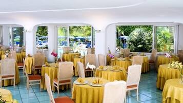 A restaurant with round tables covered in yellow tablecloths, wicker chairs, and floral centerpieces.