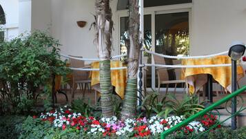 Ein Patio mit Tischen, die mit gelben Tischdecken bedeckt sind, umgeben von Pflanzen und Blumen.