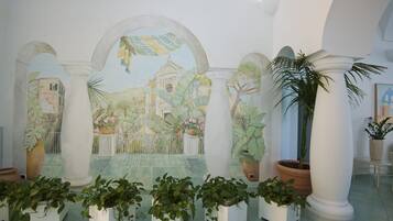 Habitación con un mural que muestra un edificio y plantas, columnas y macetas.