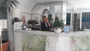 A hotel reception desk with a large potted plant, a framed photograph, and a guest review award sign.