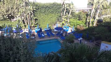 A pool area with blue lounge chairs and umbrellas, surrounded by dense greenery.