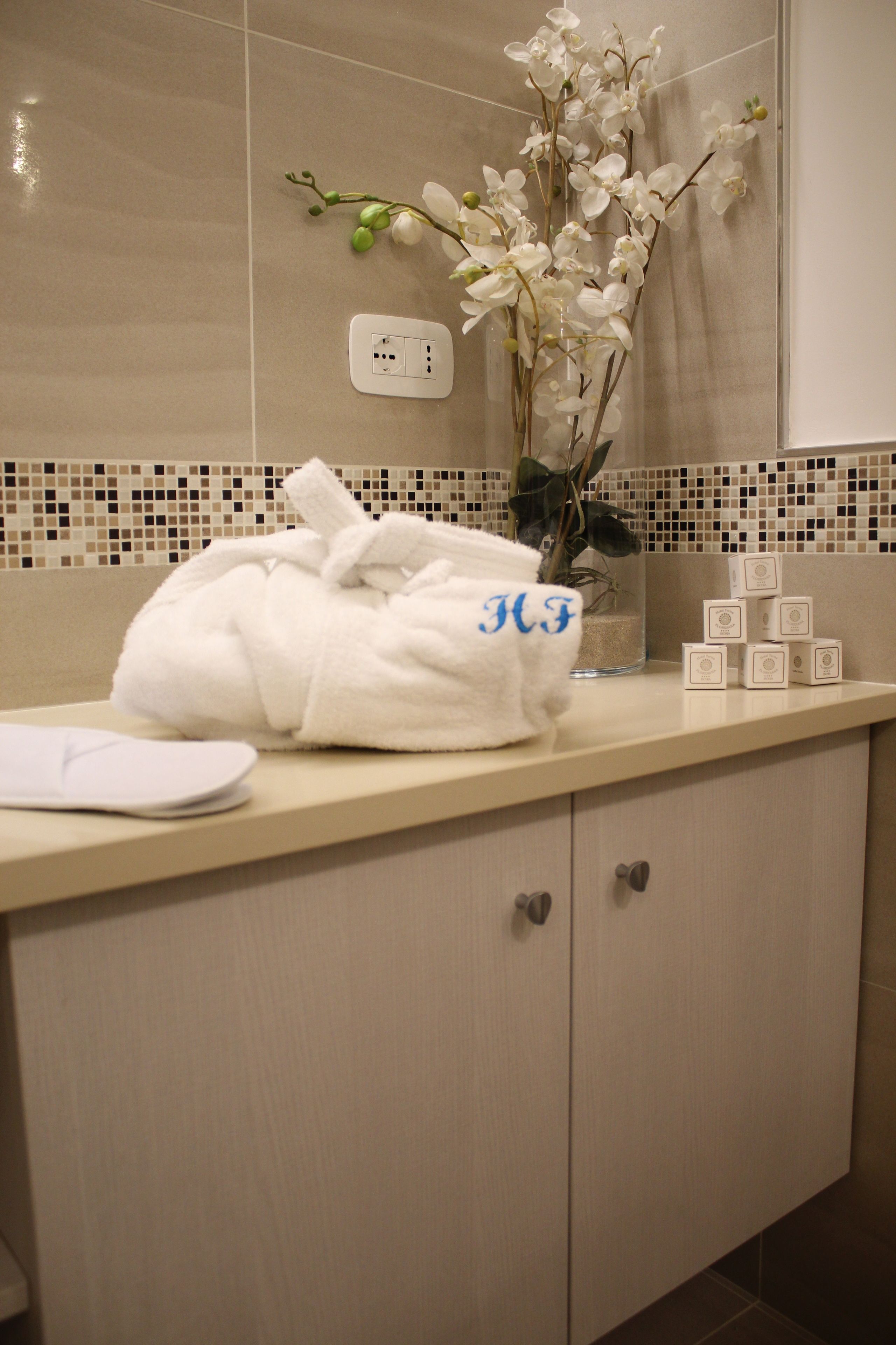 A bathroom with a white towel, a vase with white flowers, and a set of toiletries on the counter.