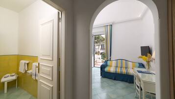 Habitación de hotel con baño, sofá, mesa de comedor y vistas al exterior.