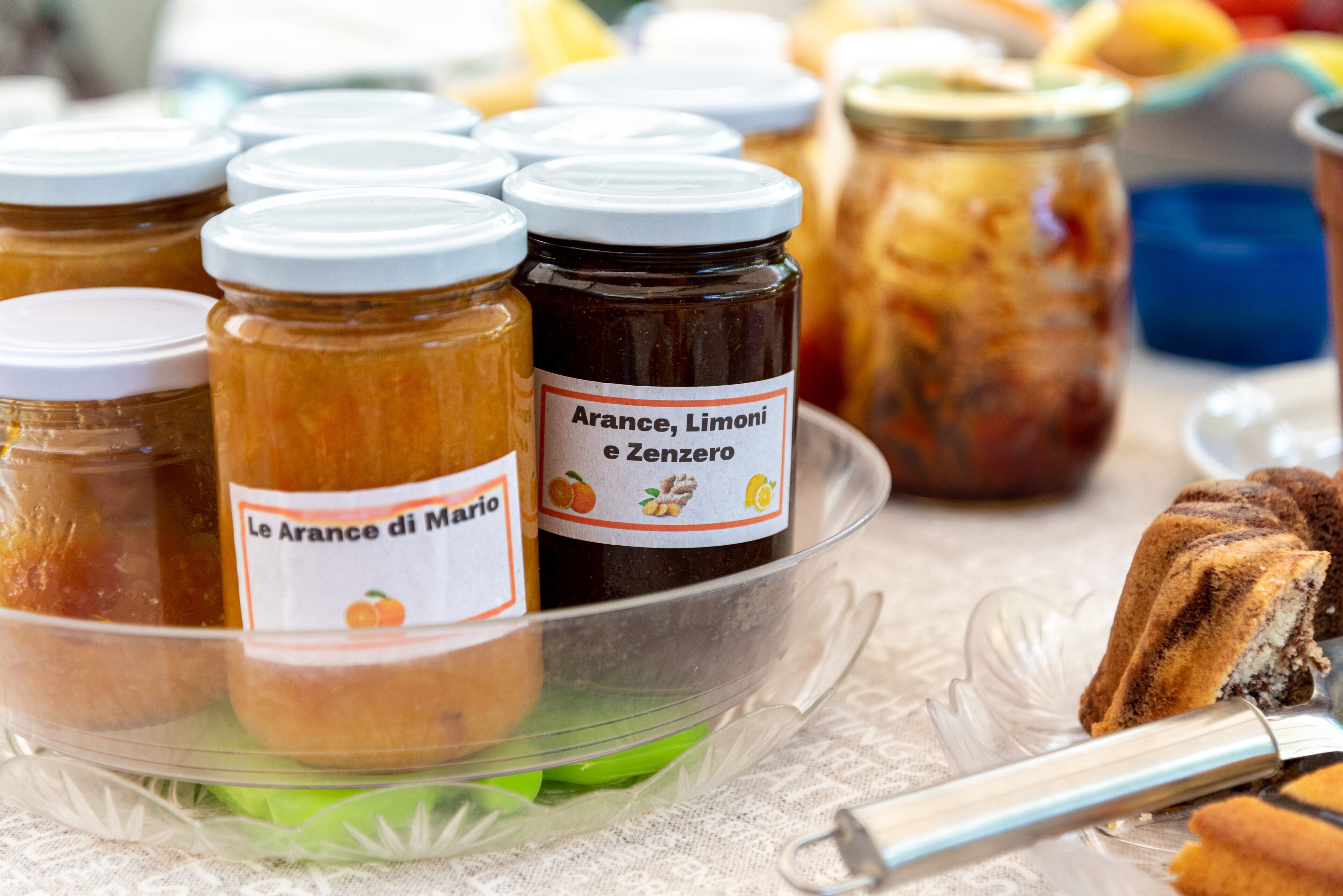 A glass display case with jars of preserved fruits and a cake on a table.