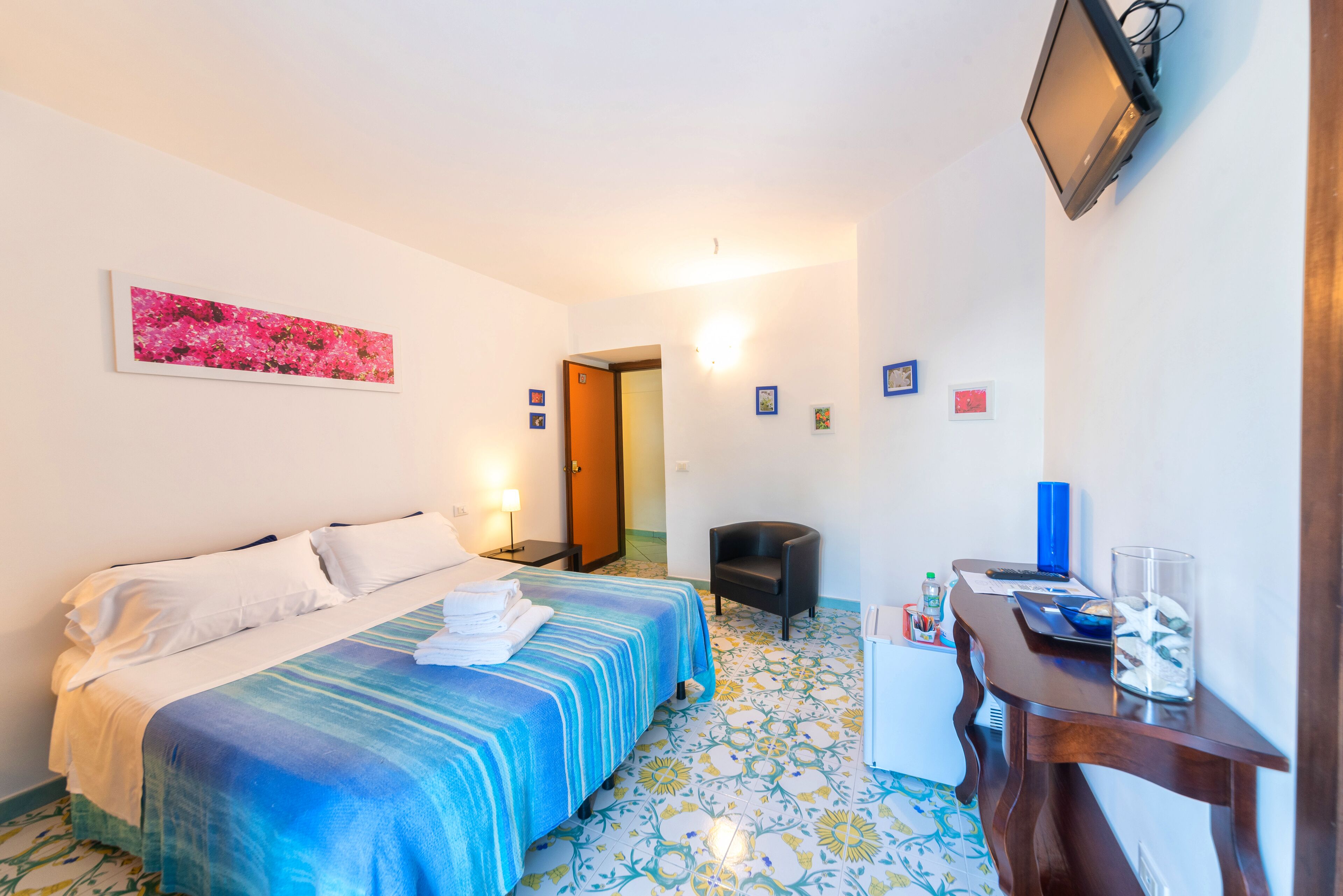 Habitación de hotel con cama, escritorio, silla, televisión y un refrigerador pequeño.