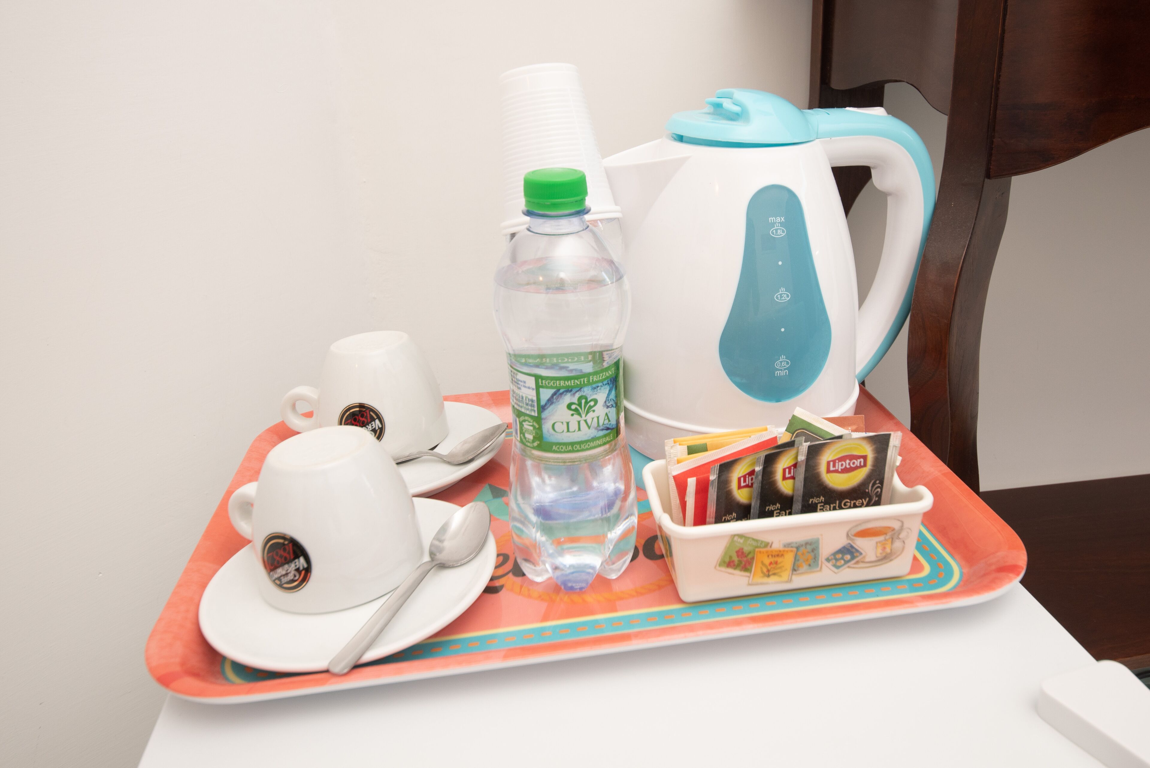 A tray with a water bottle, a kettle, cups, a spoon, and a box of tea bags.