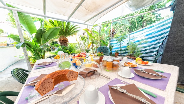 An outdoor dining area with a table set for a meal, surrounded by tropical plants and a striped awning. - Maison Twentyfive (Ischia)