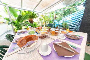 An outdoor dining area with a table set for a meal, surrounded by tropical plants and a striped awning. - Maison Twentyfive (Ischia)