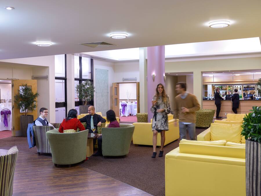 A modern lobby with yellow seating areas, a reception desk, and a bar.
