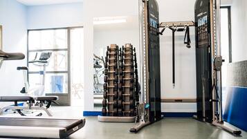 Un gimnasio con equipo de ejercicio, cinta de correr y pared espejada.