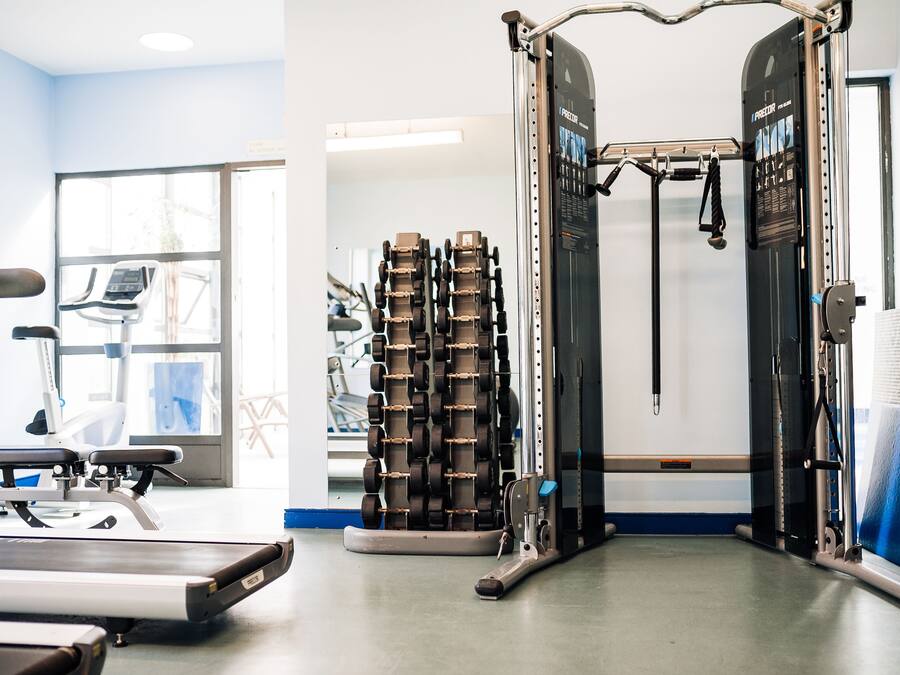 Un gimnasio con equipo de ejercicio, cinta de correr y pared espejada.