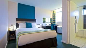 A hotel room with a bed, desk, chair, and a bathroom visible through an open door.