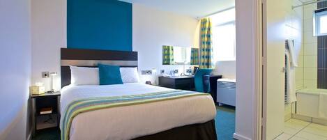 A hotel room with a bed, desk, chair, and a bathroom visible through an open door.
