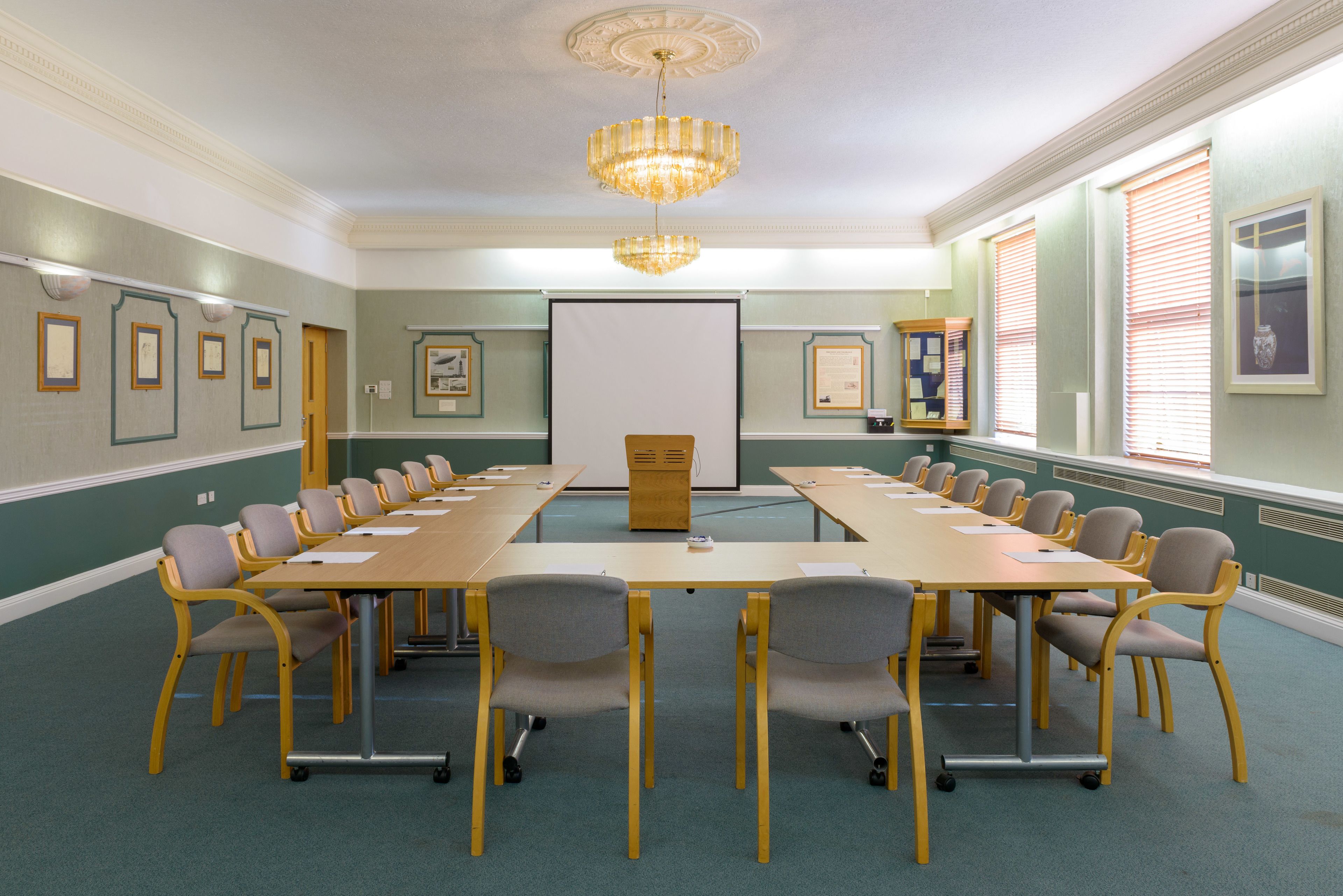 A conference room with a long table, chairs, a projector screen, and framed pictures on the walls.