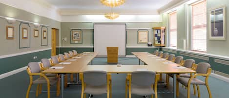 A conference room with a long table, chairs, a projector screen, and framed pictures on the walls.