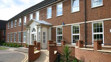 A two-story brick building with a central entrance, large windows, and a small garden area.