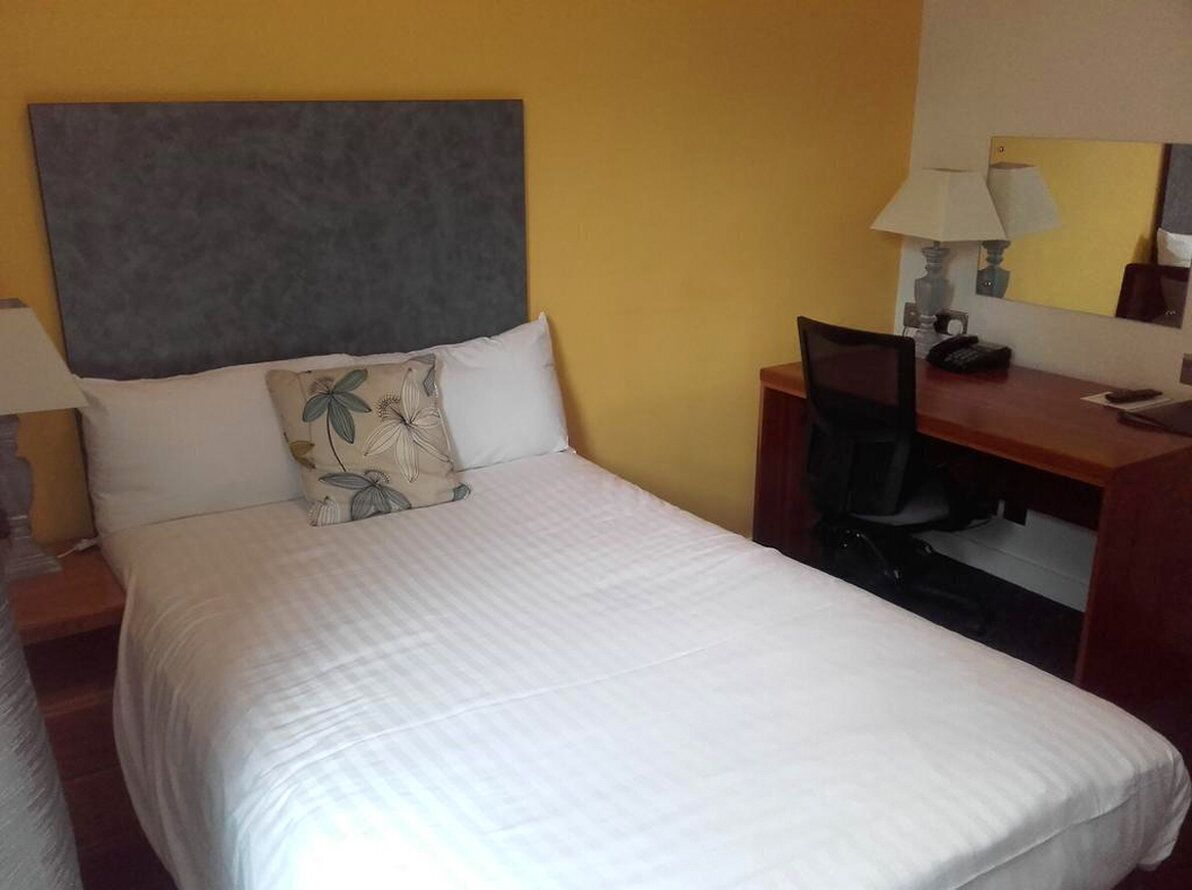 A hotel room with a bed, a desk, a chair, a lamp, and a telephone.