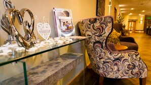 A reception area with a glass display case containing decorative items, a brochure stand, and a patterned armchair. - Mitchell Hall (Bedford)