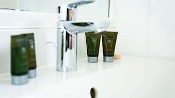 Un lavamanos con dos botellas verdes etiquetadas como 'Basic Earth Botanicals Body Wash' y 'Champú'.