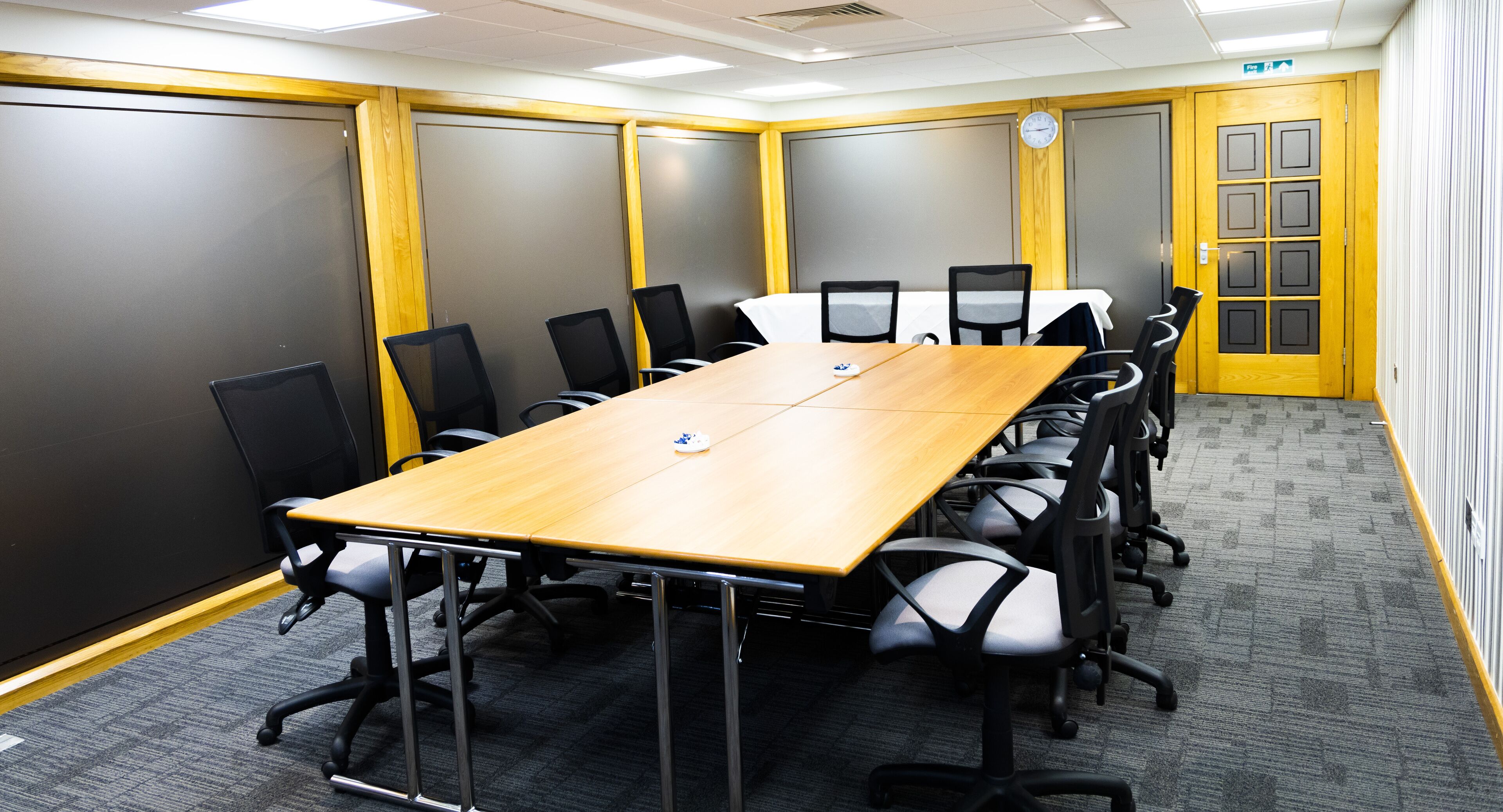 A conference room with a long table, black chairs, and a clock on the wall.