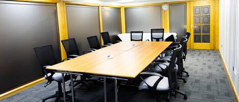 A conference room with a long table, black chairs, and a clock on the wall.