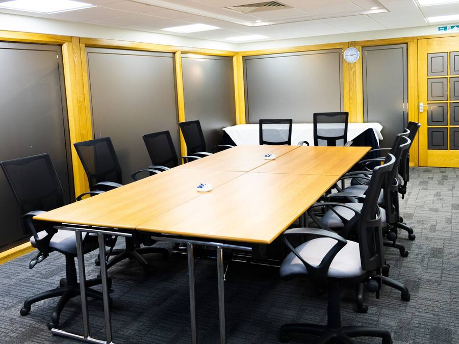 A conference room with a long table, black chairs, and a clock on the wall.