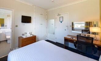 Una habitación de hotel con cama, escritorio con silla, televisión, espejo y baño con inodoro y lavamanos.