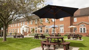 A brick building with picnic tables and umbrellas in a grassy area. - Mitchell Hall (Bedford)