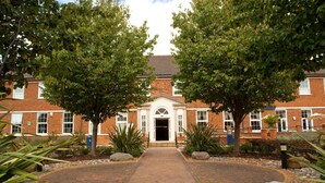 A brick building with a central entrance, surrounded by a paved pathway and landscaped with trees and rocks. - Mitchell Hall (Bedford)