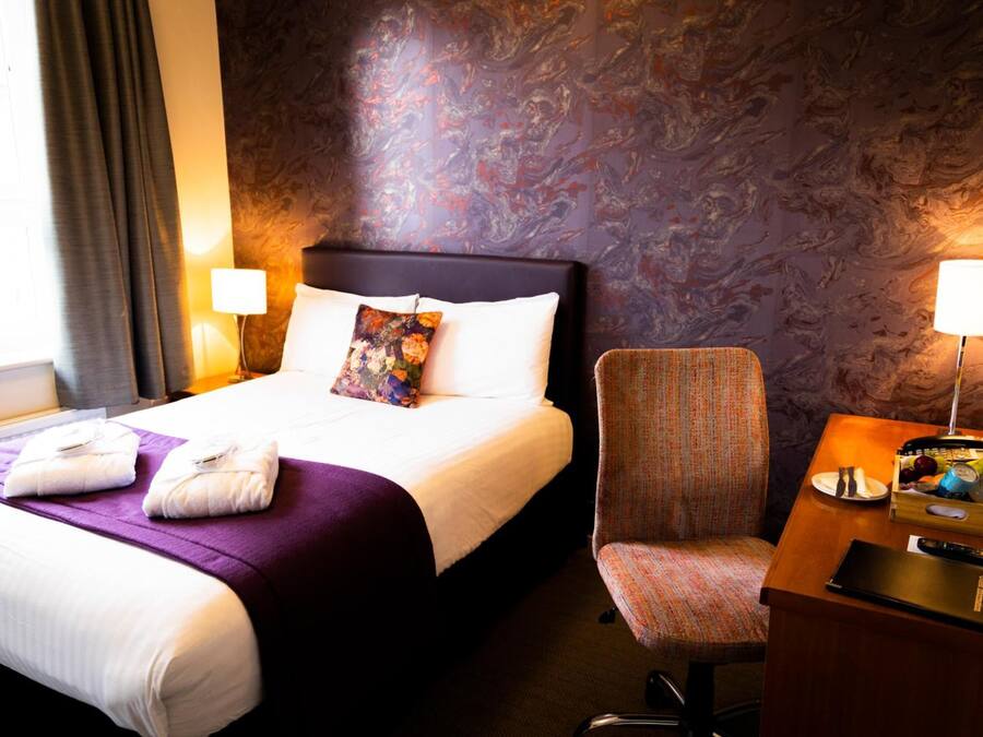 Ein Hotelzimmer mit Bett, Stuhl, Schreibtisch mit Lampe und Nachttisch.