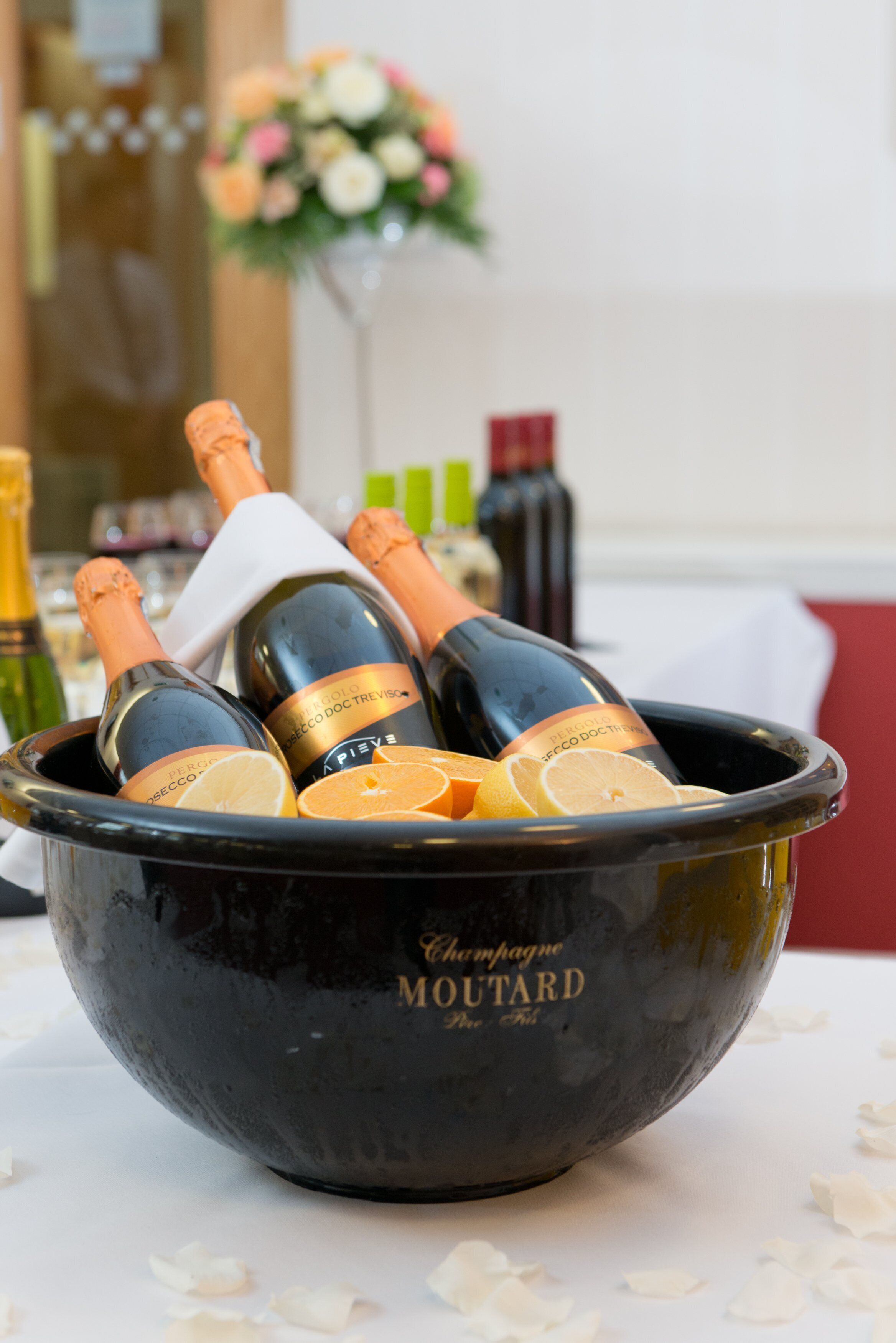 A black bowl containing champagne bottles and orange slices on a table.