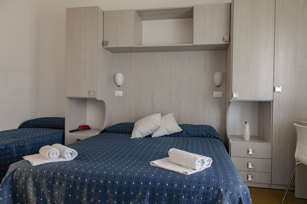 Une chambre d’hôtel avec deux lits, une armoire, une table de chevet avec une lampe et une chaise.