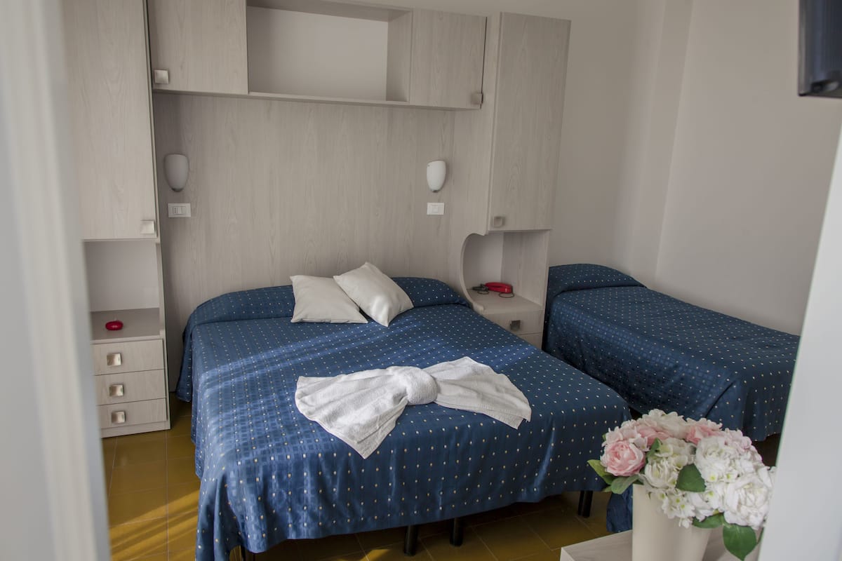 Une chambre d’hôtel avec deux lits, une table de chevet, une commode et un vase avec des fleurs.