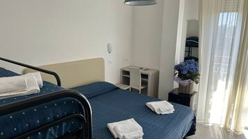 Quarto de hotel com duas camas, uma escrivaninha, uma cadeira, um abajur e uma janela com cortinas.