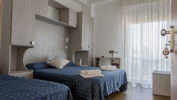Ein Hotelzimmer mit zwei Betten, einem Schreibtisch, einem Stuhl, einem kleinen Tisch mit einer Vase und einem Fenster mit Vorhängen.