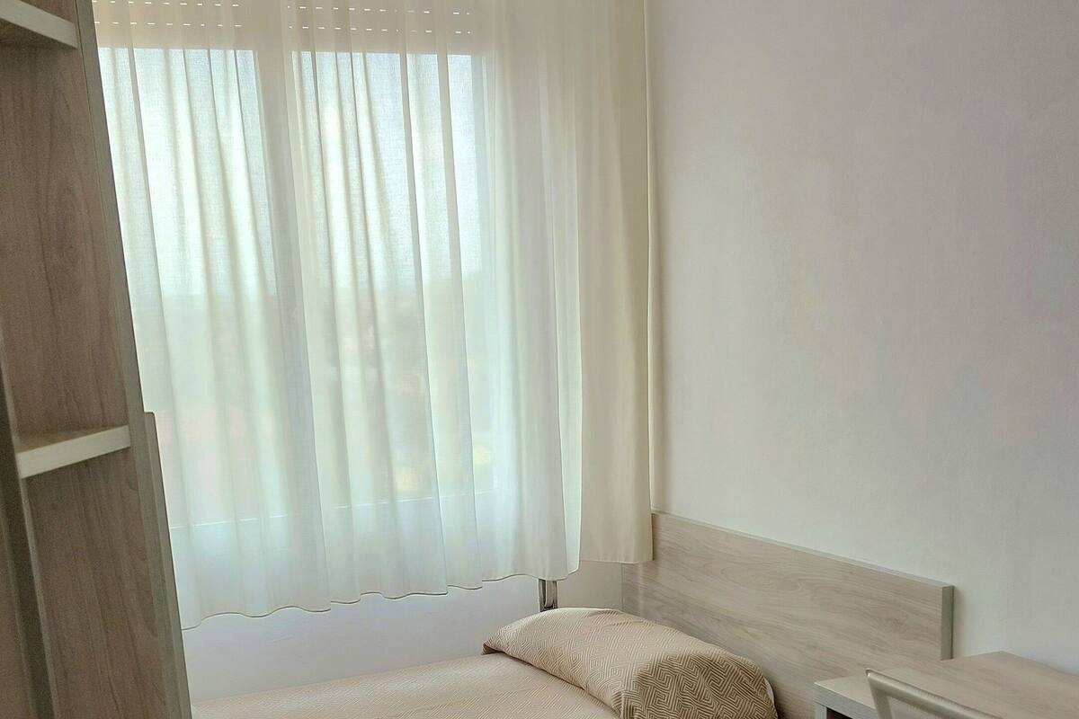 Une petite pièce, bien rangée, avec un lit, un bureau et une chaise.
