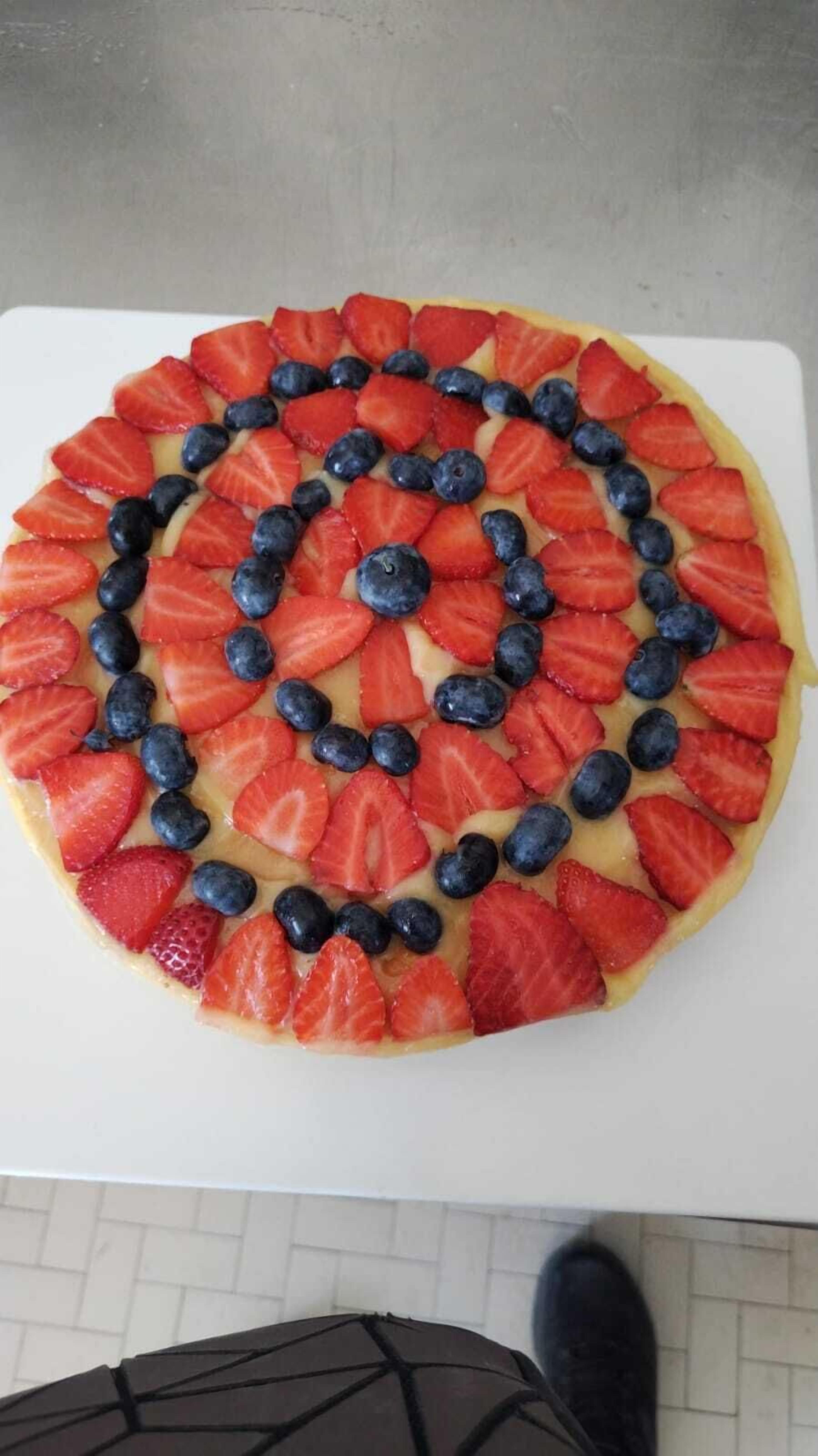 Uma tarte de fruta redonda com um padrão espiral de morangos e mirtilos sobre um prato branco.