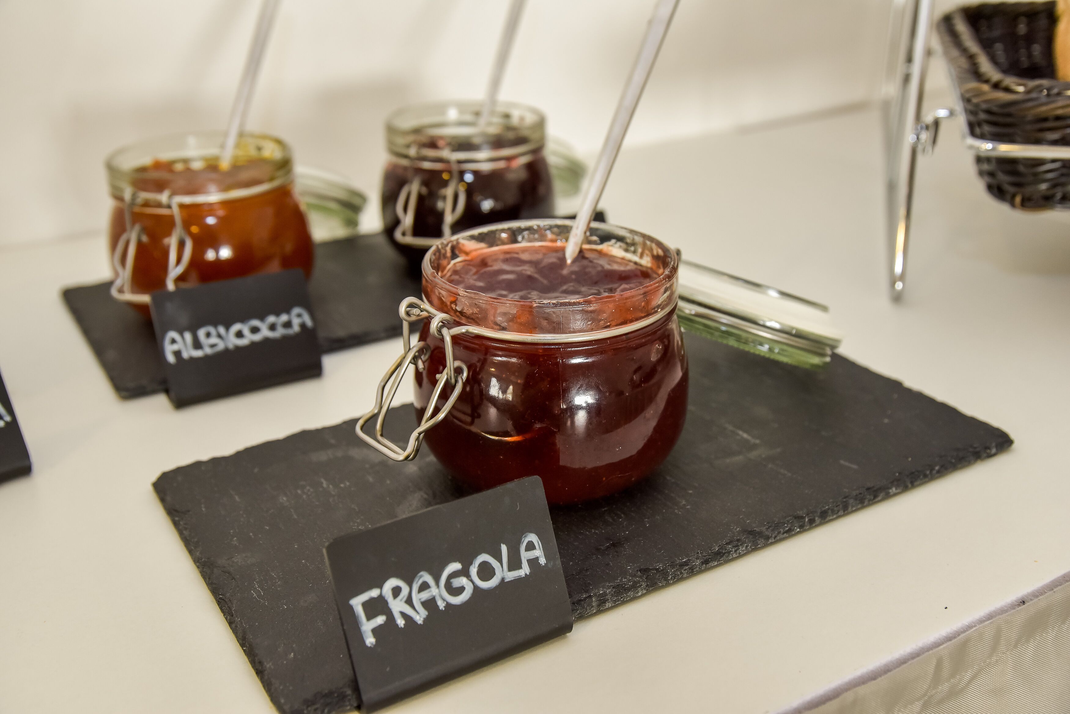 Jars of jam labeled 'ALBYCOCCA' and 'FRAGOLA' on a counter.