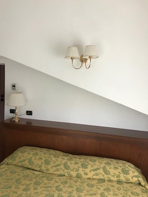 Een slaapkamer met een houten hoofdbord, een bed met beddengoed met bloemenprint en twee wandlampen.