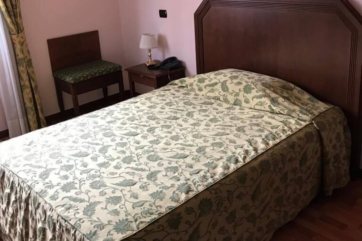 A bedroom with a bed, a nightstand, a chair, a lamp, and a wall-mounted light fixture.