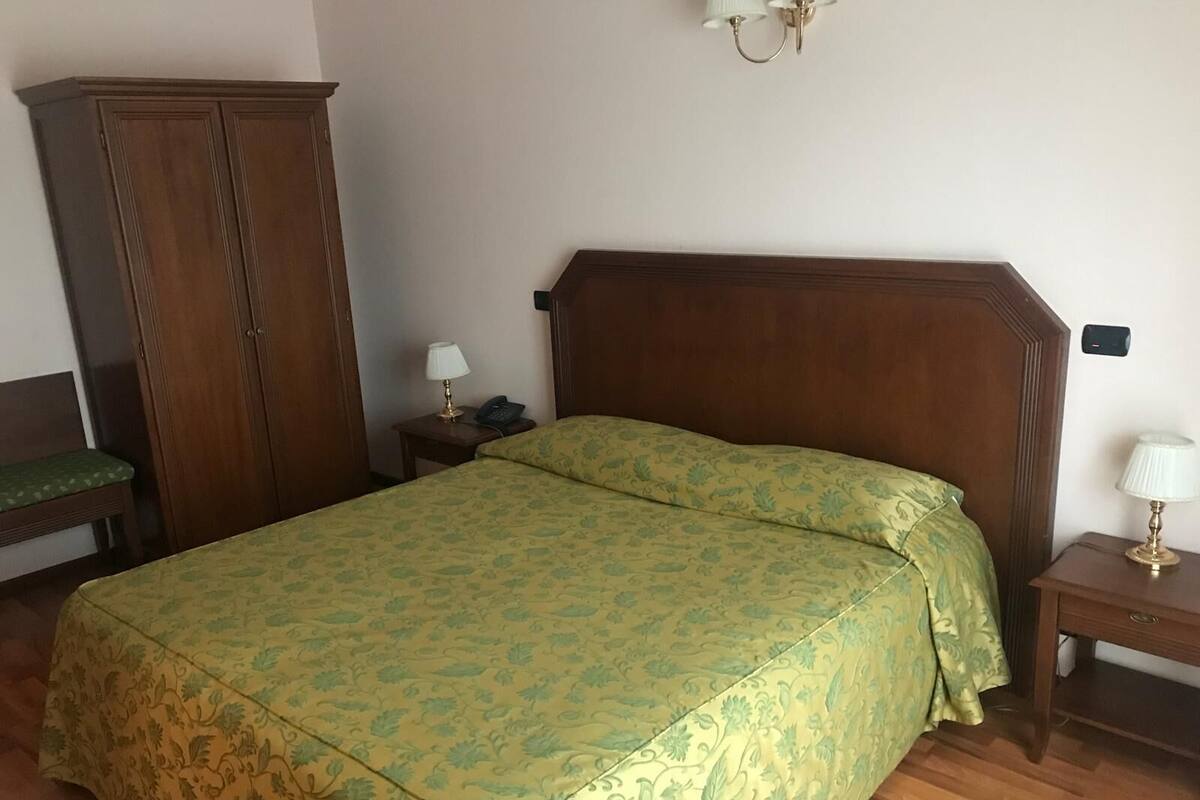 A neatly arranged bedroom with a bed, a wardrobe, a bedside table with a lamp, and a wall-mounted light fixture.