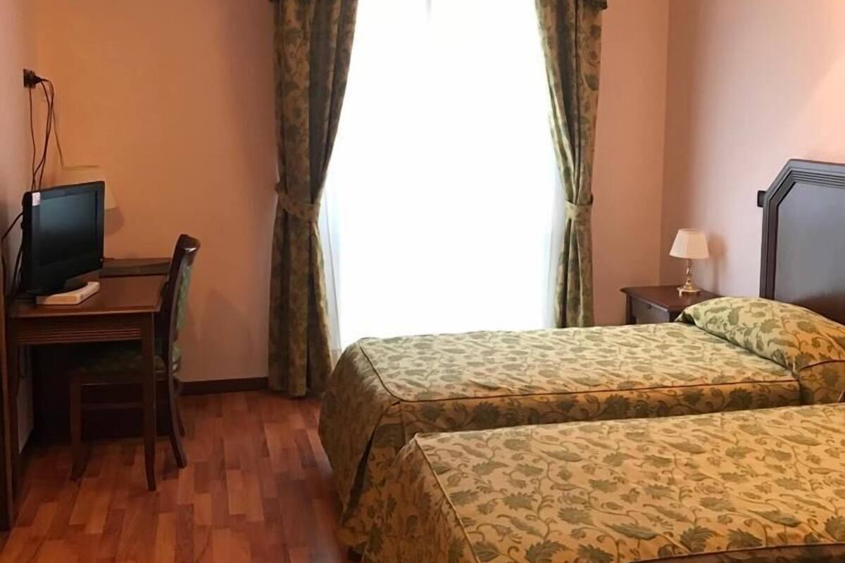 A hotel room with two beds, a desk with a computer, and a window with curtains.