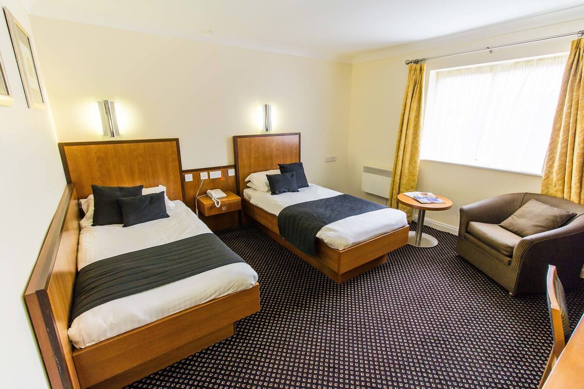 A hotel room with two wooden beds, a small round table, a sofa, and a window with curtains.