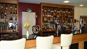 A bar area with multiple shelves of bottles, a bar counter, and two white bar stools. - Padbrook Park (Cullompton)