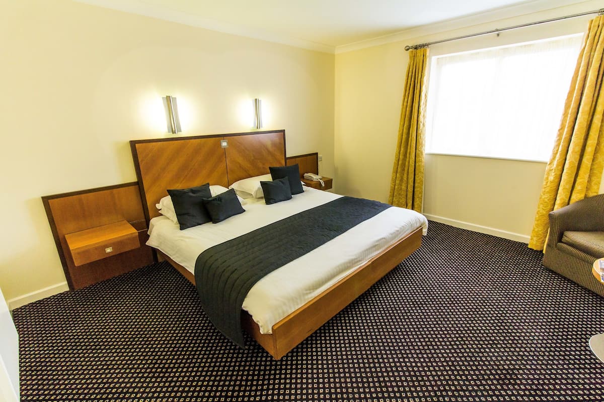 A hotel room with a large bed, a nightstand, a chair, and a window with curtains.
