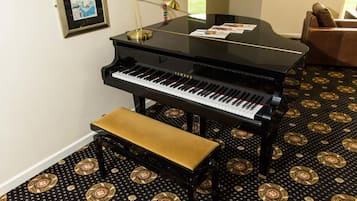 A grand piano in a room with patterned carpet, a bench, a lamp, and a framed picture on the wall.
