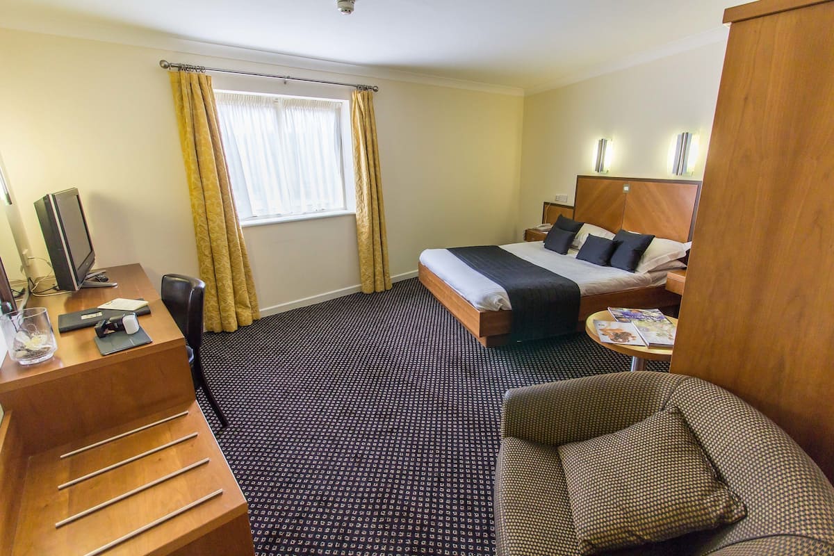 A hotel room with a bed, a desk, a chair, a small table, and a window with curtains.